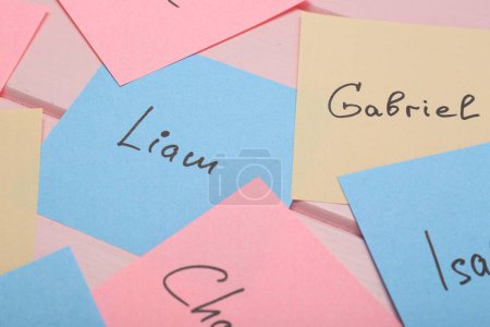 Paper stickers with different names on pink wooden table, closeup. Choosing baby's name