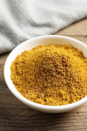 Photo for Dry curry powder in bowl on wooden table, closeup - Royalty Free Image