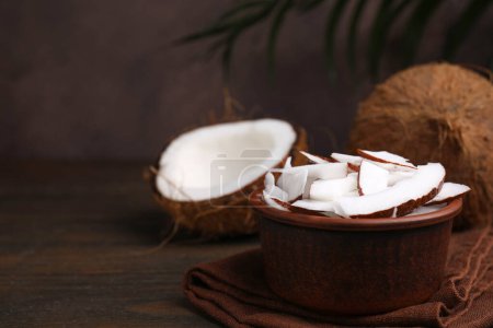Coconut pieces in bowl and nuts on wooden table, space for text
