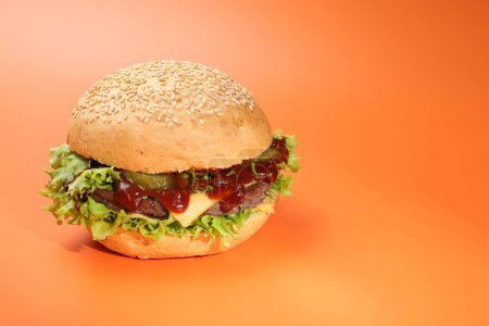 Delicious cheeseburger with lettuce, pickle, ketchup and patty on coral background. Space for text