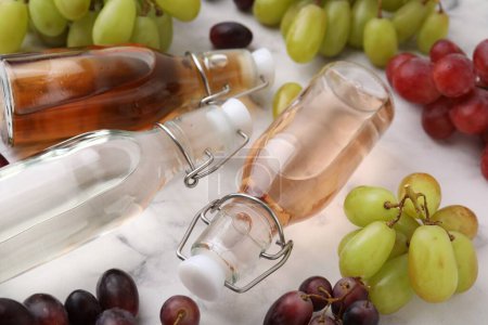 Verschiedene Essigsorten in Flaschen und Trauben auf hellem Tisch, Nahaufnahme