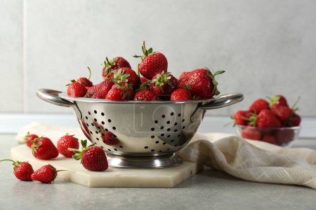 Metal colander with fresh strawberries on grey countertop