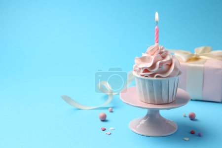 Photo for Delicious birthday cupcake with burning candle and sprinkles on light blue background, closeup. Space for text - Royalty Free Image