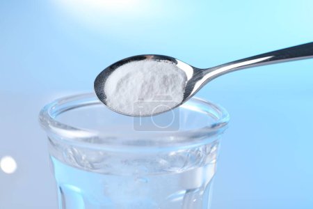 Adding baking soda into glass of water on light blue background, closeup