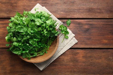 Fresh coriander in bowl on wooden table, top view. Space for text