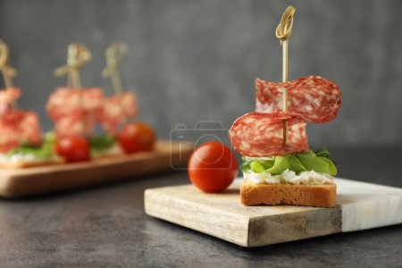 Photo for Tasty canapes with salami, greens, cream cheese and tomatoes on grey table, closeup. Space for text - Royalty Free Image