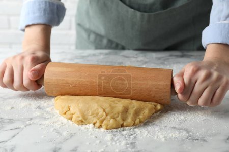 Making shortcrust pastry. Woman rolling raw dough at white marble table, closeup