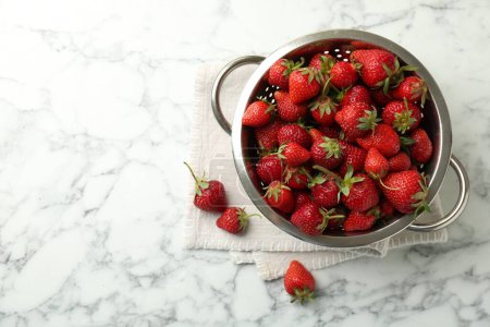 Metal colander with fresh strawberries on white marble table, top view. Space for text