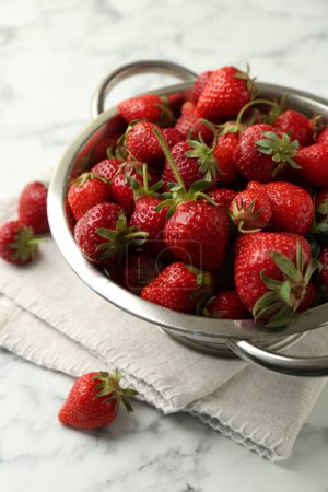 Metal colander with fresh strawberries on white marble table
