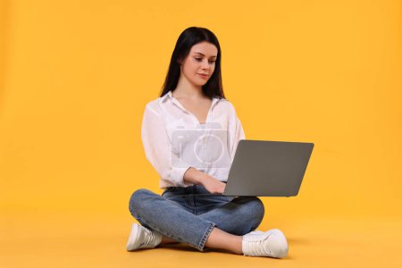 Student with laptop sitting on yellow background