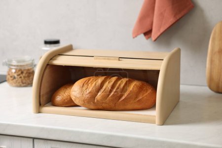 Brotkorb aus Holz mit frisch gebackenen Broten auf weißem Marmortisch in der Küche