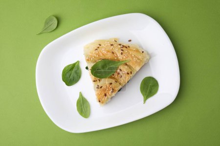 Piece of delicious puff pastry with spinach on green background, top view
