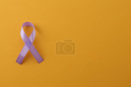 Violet awareness ribbon on orange background, top view. Space for text
