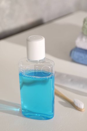Foto de Botella de enjuague bucal y cepillo de dientes sobre mesa blanca en baño - Imagen libre de derechos