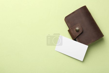 Porte-cartes de visite en cuir avec carte blanche sur fond vert clair, vue de dessus. Espace pour le texte
