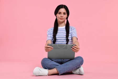 Student with laptop sitting on pink background