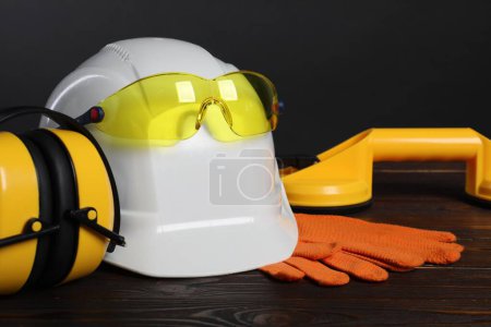 Hard hat, goggles, earmuffs, suction lifters and protective gloves on wooden surface against gray background