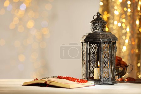 Arabic lantern, Quran, misbaha and dates on table against blurred lights, space for text
