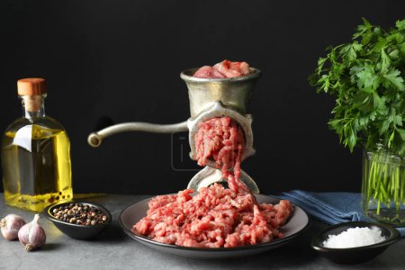 Manuelle Fleischmühle mit Rinderhackfleisch, Gewürzen, Öl und Petersilie auf grauem Tisch