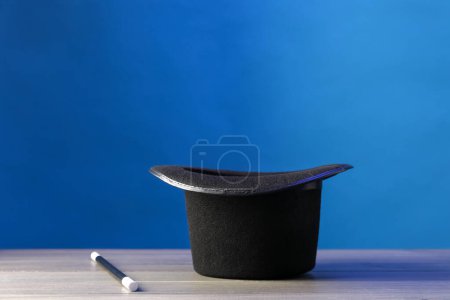 Zauberhut und Zauberstab auf Holztisch vor blauem Hintergrund, Platz für Text