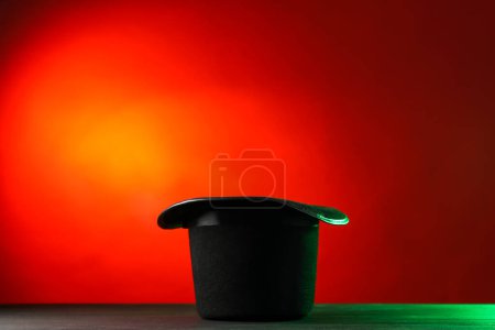 Magician's hat on black wooden table against color background, space for text