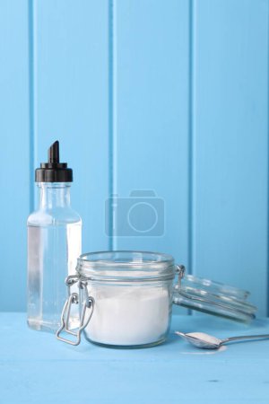 Productos de limpieza natural. Vinagre en botella, bicarbonato de sodio y cuchara sobre mesa de madera azul claro