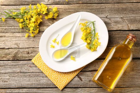 Rapsöl in Soße, Flasche und schönen gelben Blumen auf Holztisch, flache Lage