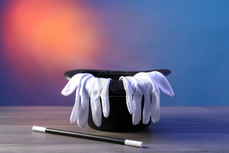 Zaubermütze, Zauberstab und Handschuhe auf Holztisch vor farbigem Hintergrund