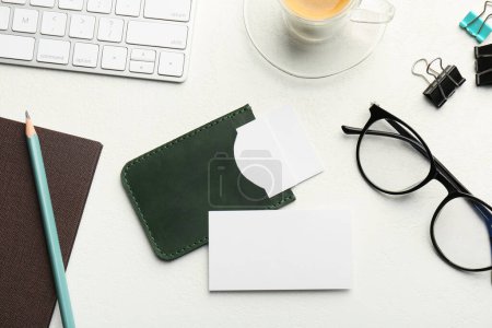 Leder-Visitenkartenetui mit Blanko-Karten, Brille, Tastatur und Schreibwaren auf weißem Tisch, flach gelegt