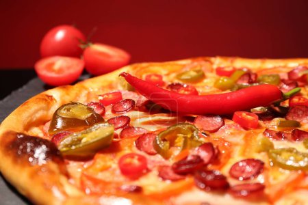 Delicious pizza Diablo, tomatoes and chili peppers against red background, closeup