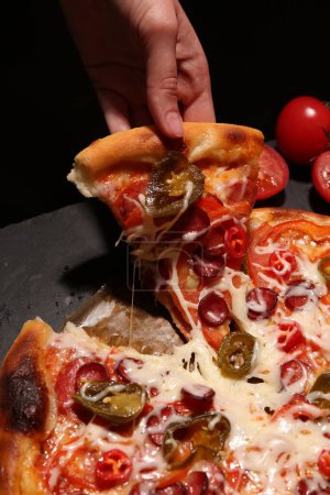 Woman taking piece of delicious pizza Diablo on black background, closeup