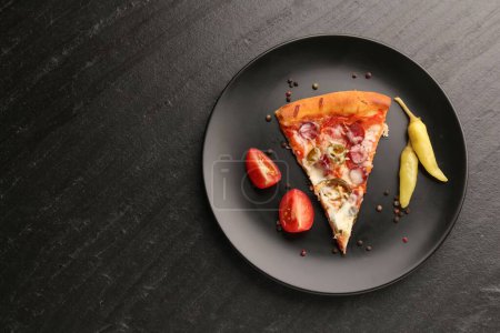 Plate with delicious pizza Diablo, pepper, tomato and peppercorns on dark textured table, top view. Space for text