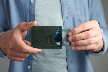 Téléchargez les photos : Homme tenant un porte-cartes en cuir avec cartes de crédit sur fond gris, gros plan - en image libre de droit