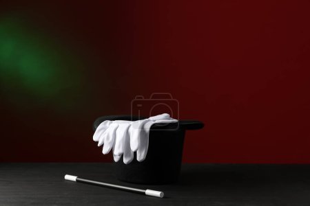 Magician's hat, wand and gloves on black wooden table against dark background