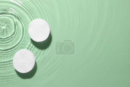 Wattepads in Mikrokellerwasser auf grünem Hintergrund, Draufsicht. Raum für Text