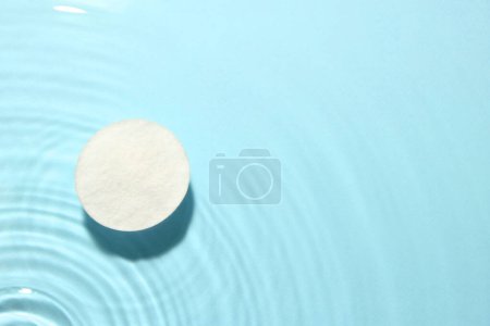 Cotton pad in micellar water on light blue background, top view. Space for text
