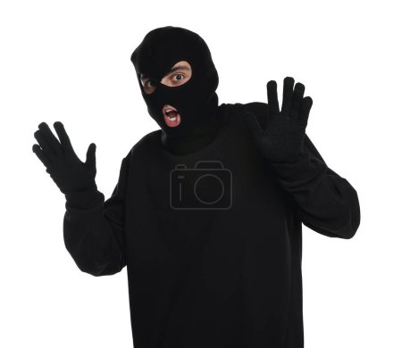 Emotional thief in balaclava raising hands on white background