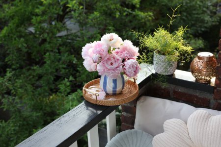 Beautiful pink peony flowers in vase and potted plant on balcony railing outdoors