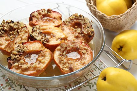 Deliciosos membrillos horneados con nueces en tazón y frutas frescas en la mesa, primer plano