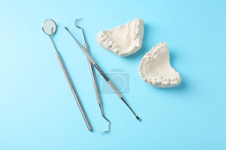 Dental model with gums and dentist tools on light blue background, flat lay. Cast of teeth