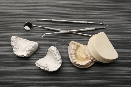 Dental models with gums and dentist tools on grey wooden table, flat lay. Cast of teeth