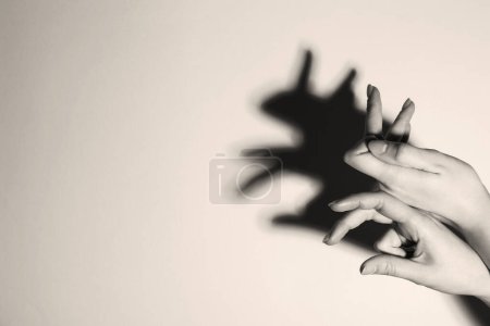 Títere de sombra. Mujer haciendo gesto de mano como conejo sobre fondo claro, primer plano con espacio para el texto. Efecto blanco y negro