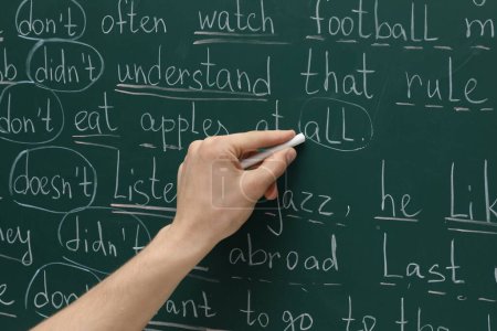 English teacher writing with chalk on green chalkboard, closeup