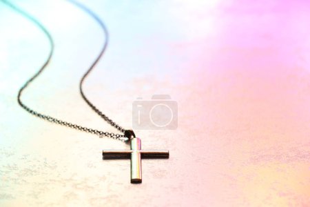 Cross with chain on textured table in color lights, closeup and space for text. Religion of Christianity