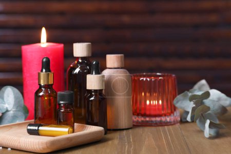 Différents produits d'aromathérapie, bougies allumées et feuilles d'eucalyptus sur table en bois