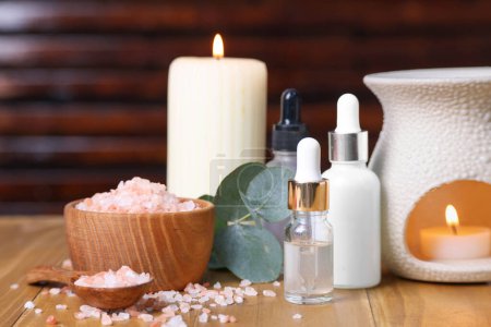 Verschiedene Aromatherapie-Produkte, brennende Kerzen und Eukalyptusblätter auf Holztisch, Nahaufnahme