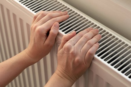 Téléchargez les photos : A woman warms hands on a radiator. Home heating. Low temperature and cold in the house. Photo closeup - en image libre de droit