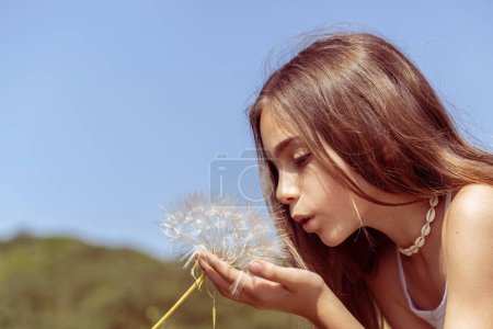 Photo for A beautiful girl in the countryside blowing on a flower in the wind with clear sky background for copy space - Royalty Free Image