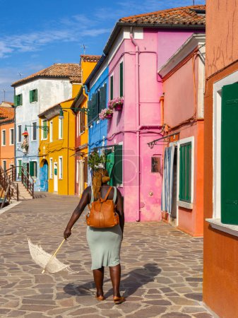 Photo for Burano, Italy - August 9, 2023; Black woman with umbrella from the back standing on the street with colorful Venetian houses - Royalty Free Image