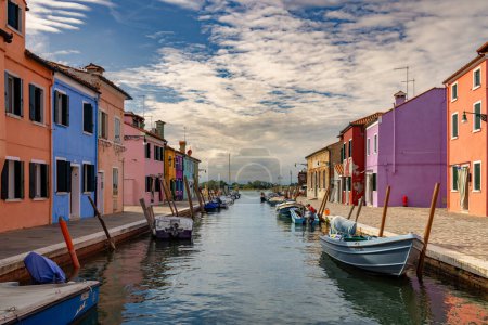 Photo for Burano, Italy - August 9, 2023; A cloudy sky meets the river water on the horizon, colorful houses on both sides of the canal and boats on the water - Royalty Free Image